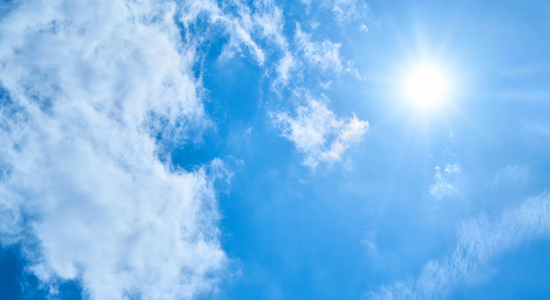 The sun shining through white clouds in a clear blue sky
