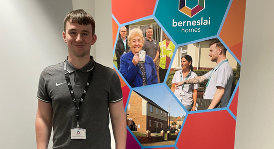 A smiling student stood in an office and in front of a Berneslai Homes pop up banner.