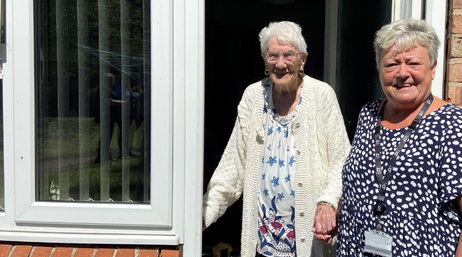 One member of staff from Berneslai Homes holding an older tenant's hand in front of their home.